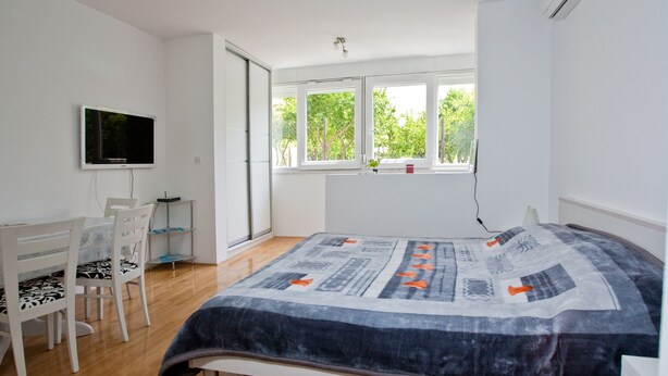 A bedroom with a bed, a desk, a chair, and a TV. There is a window with a view of trees. - 4* studio apartment, simple and modern in the beautiful city of Split (Split)