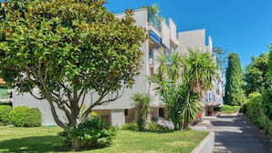 Un edificio moderno con varios balcones, rodeado de abundante vegetación y un césped cuidado.