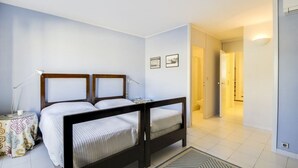 Un dormitorio con dos camas, una mesita de noche con lámpara, un mantel con estampado y una alfombra.