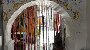 An interior hallway with an archway decorated with colorful ribbons, a statue of a cat, and a patterned sofa. - Chelitos Backpacker (Cusco)