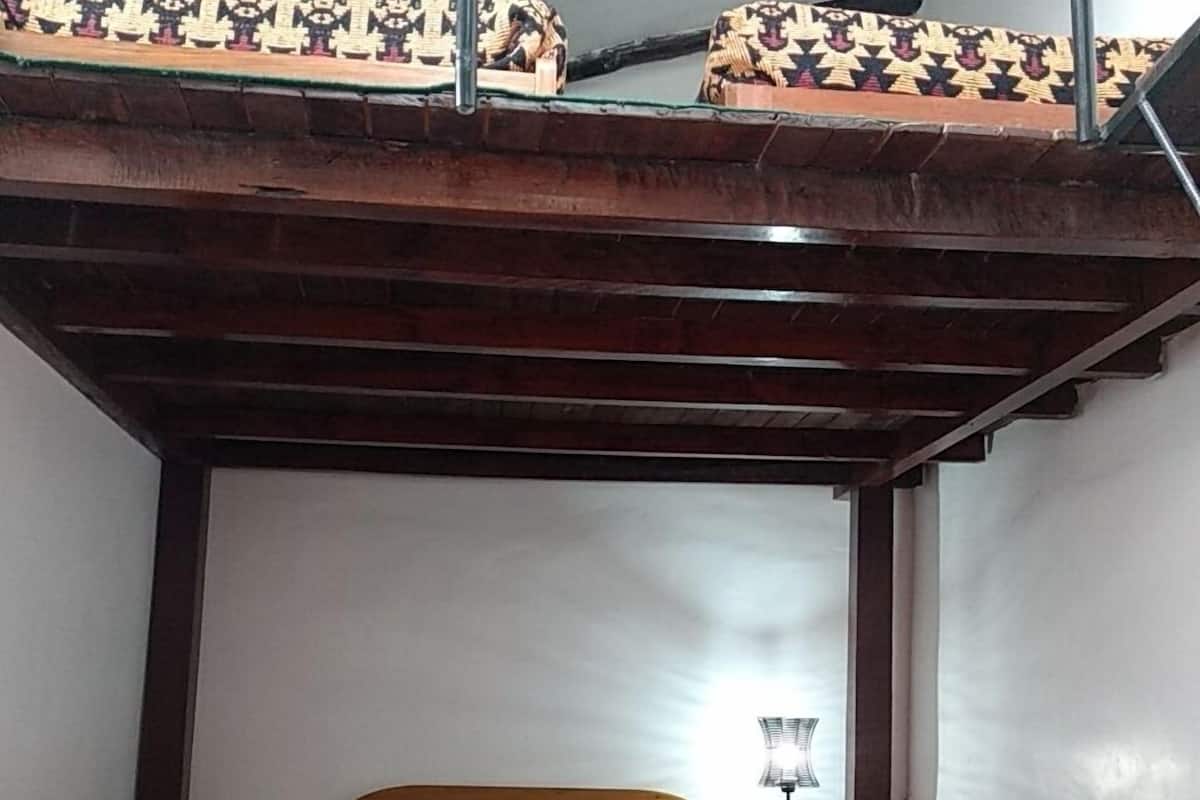 A bunk bed with a patterned bedspread and pillows, a bedside lamp, and a small wooden nightstand.