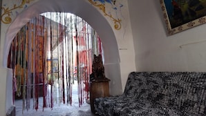 An arched doorway with colorful hanging decorations, a rustic wooden statue, and a patterned sofa. - Chelitos Backpacker (Cusco)