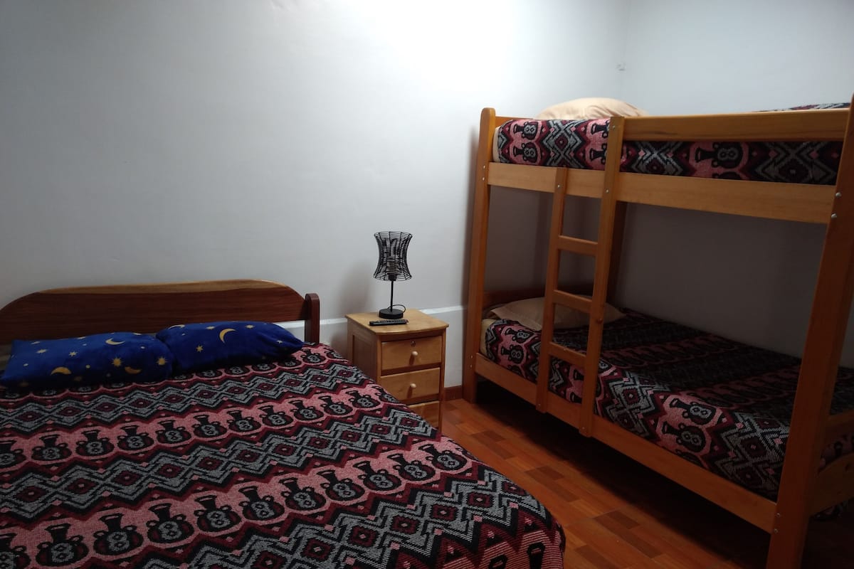 A room with two bunk beds, a small bedside table with a lamp, and a patterned bedspread.