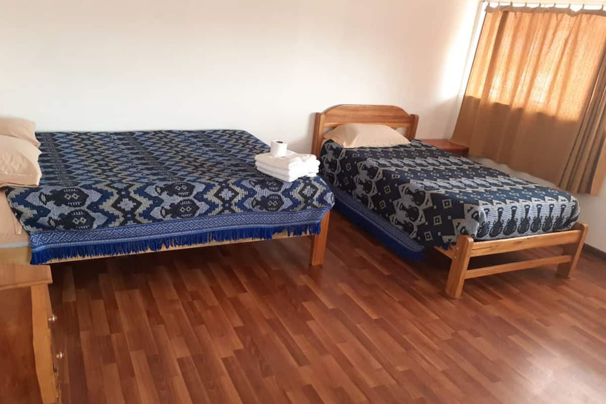 Two wooden beds with patterned bedding, a wooden floor, and a window with curtains.