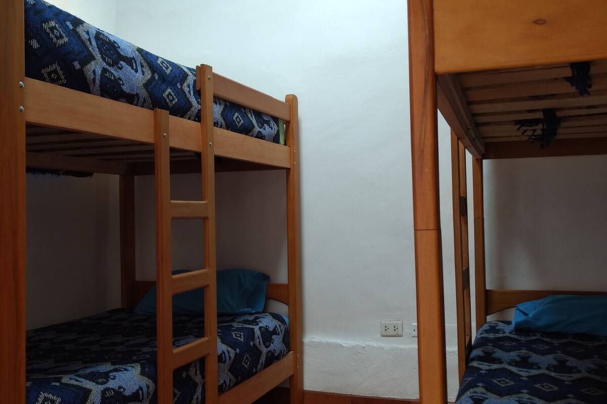 A room with two bunk beds, wooden flooring, and a white wall.