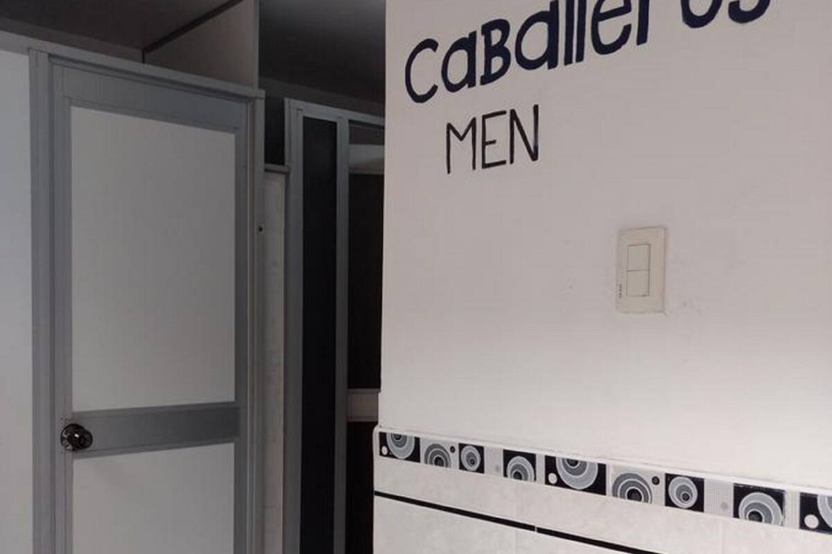 A bathroom with a white door, a tiled wall with a decorative border, and the text "Caballeros MEN" on the wall.