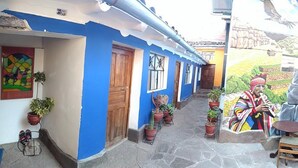 A courtyard with a mural, potted plants, and a small table and chair. - Chelitos Backpacker (Cusco)
