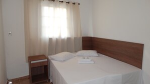A neatly made bed with white linens, a wooden nightstand, and a window with sheer curtains. - Practic Pousada (Aparecida)
