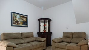 A living room with two beige sofas, a dark wooden cabinet, and a framed painting on the wall. - Practic Pousada (Aparecida)