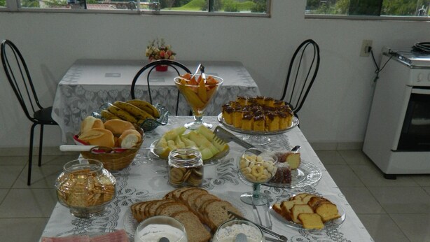 A buffet table with various food items and utensils. - Practic Pousada (Aparecida)