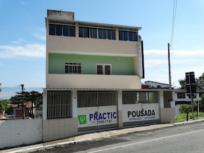 Un bâtiment à deux étages, doté d’une façade verte et blanche, avec des panneaux indiquant « PRACTIC » et « POUSADA », ainsi que les numéros de téléphone.