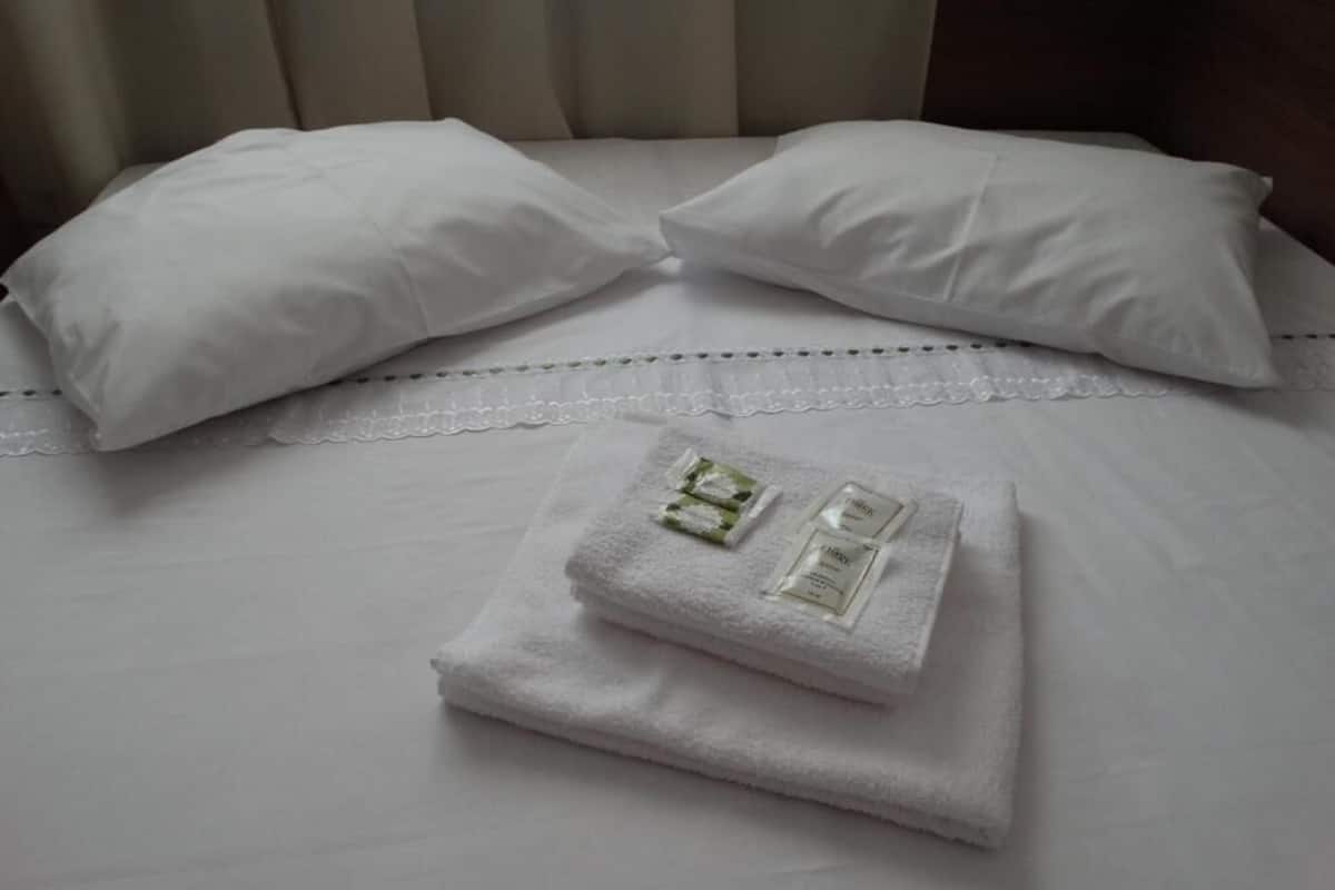 A neatly made bed with white linens, two pillows, and a folded towel with toiletries.