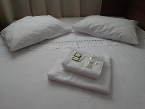 Un lit bien fait, avec du linge de lit blanc, deux oreillers et une serviette pliée, accompagnée d’articles de toilette.