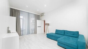 A modern living room with a teal sofa, a white console table, and a large window with curtains. - Novus apartments in Odesa (Odes'ka oblast)