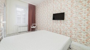 A bedroom with a bed, a TV mounted on the wall, a window with curtains, and a radiator. - Novus apartments in Odesa (Odes'ka oblast)