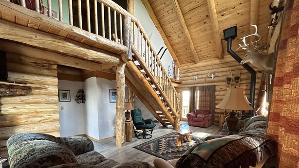 L’intérieur d’une cabane en rondins, avec un escalier en bois, une cheminée, un canapé et un fauteuil.