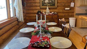 L’intérieur d’un chalet en bois présente une table à manger dressée pour quatre personnes, agrémentée de sets de table en fibres tressées, de bougies et de décorations festives.