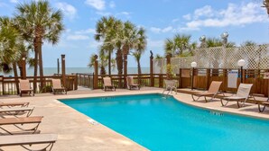 A pool area with lounge chairs, palm trees, and a view of the ocean. - Sun N Sand 603 (Myrtle Beach)