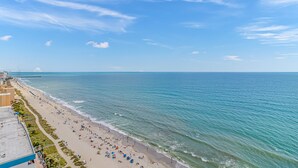 A beach with a clear sky, a long stretch of sand, and a few buildings along the shore. - The Palace 202 (Myrtle Beach)