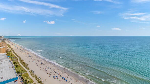 A beach with a clear sky, a long stretch of sand, and a few buildings along the shore. - The Palace 105 (Myrtle Beach)