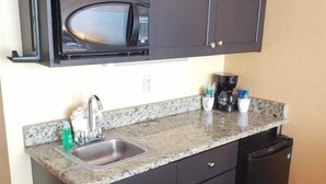 Una cocina compacta con armarios oscuros, un lavamanos de acero inoxidable, un microondas, una cafetera y un lavavajillas.