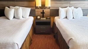 Una habitación de hotel con dos camas, una mesita de noche con lámparas y un cabecero de madera.