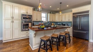 A kitchen with white cabinets, a black refrigerator, and a wooden island with stools. - Channel Marker (Murrells Inlet)