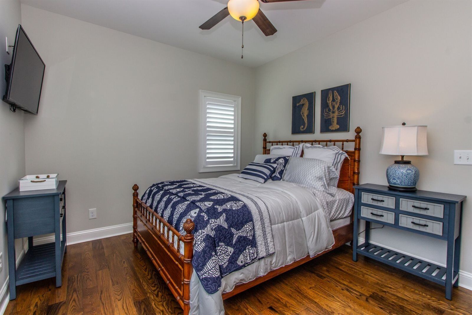 A bedroom with a wooden bed, a nightstand, a dresser, a ceiling fan, and artwork on the wall.