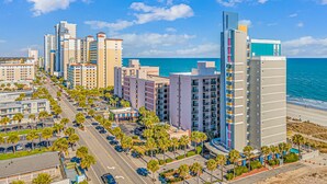 Un paysage urbain côtier avec de hauts immeubles, un ciel bleu dégagé et une plage en arrière-plan.