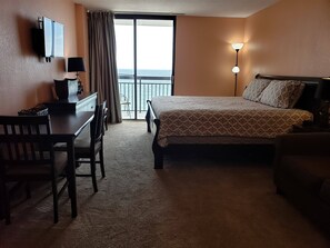 A hotel room with a bed, desk, chair, TV, and a balcony with a view. - Sun N Sand 811 (Myrtle Beach)