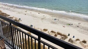 A beach with people sunbathing and swimming, a wooden fence, and a clear view of the ocean.