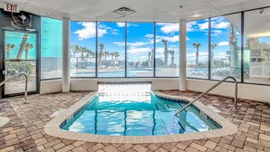 Piscina interior con vistas despejadas a palmeras y un cielo azul a través de amplios ventanales.