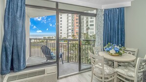 Un balcon avec vue sur l’océan et les bâtiments, une table avec des chaises et un vase de fleurs.