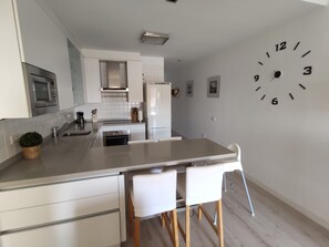 Een moderne keuken met een centraal eiland, witte kastjes en een wandklok.