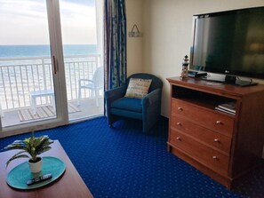 Ein Zimmer mit Balkon, Fernseher, Stuhl und Holzkommode.