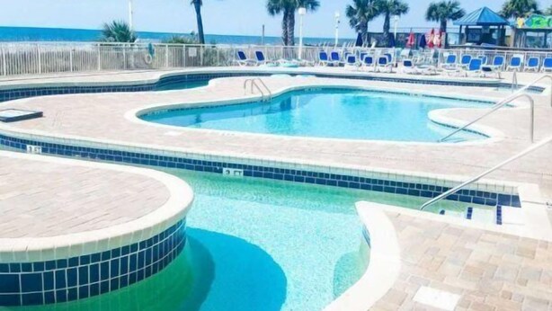 A pool area with a 3 FT depth marker, lounge chairs, palm trees, and a view of the ocean. - Bay Watch 1438 (North Myrtle Beach)