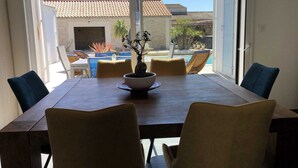 Een eetgedeelte met een tafel en stoelen, een potplant en een uitzicht op een zwembad en een gebouw op de achtergrond.