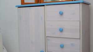 A white wardrobe with blue trim and six drawers, topped with a wooden mirror. - 1bed Cottage Sleeps 2 - Enclosed Garden, Pets, Bbq (Helston)