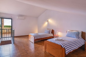 Quarto com duas camas de madeira, uma mesinha e uma varanda.