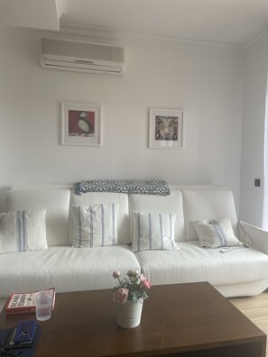 Um sofá branco com almofadas listradas, um cobertor estampado e duas obras de arte emolduradas na parede.