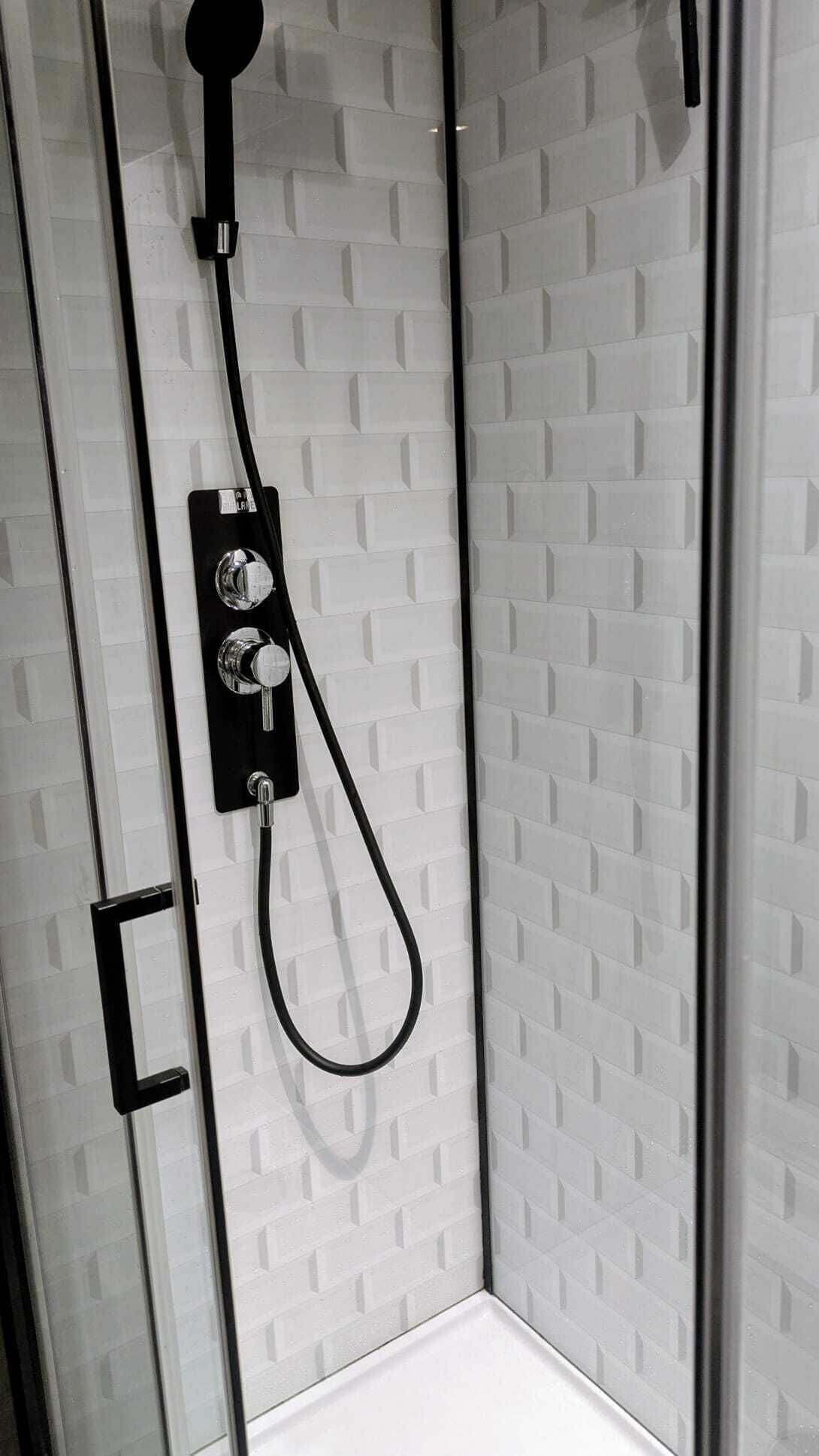 A glass-enclosed shower with a black hose and control panel.