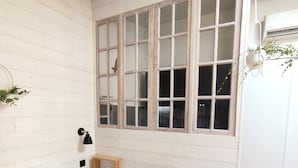 A bedroom with a bed, a window with wooden frames, a wall-mounted lamp, and a small wooden shelf. - Appartement Lila (Carcassonne)