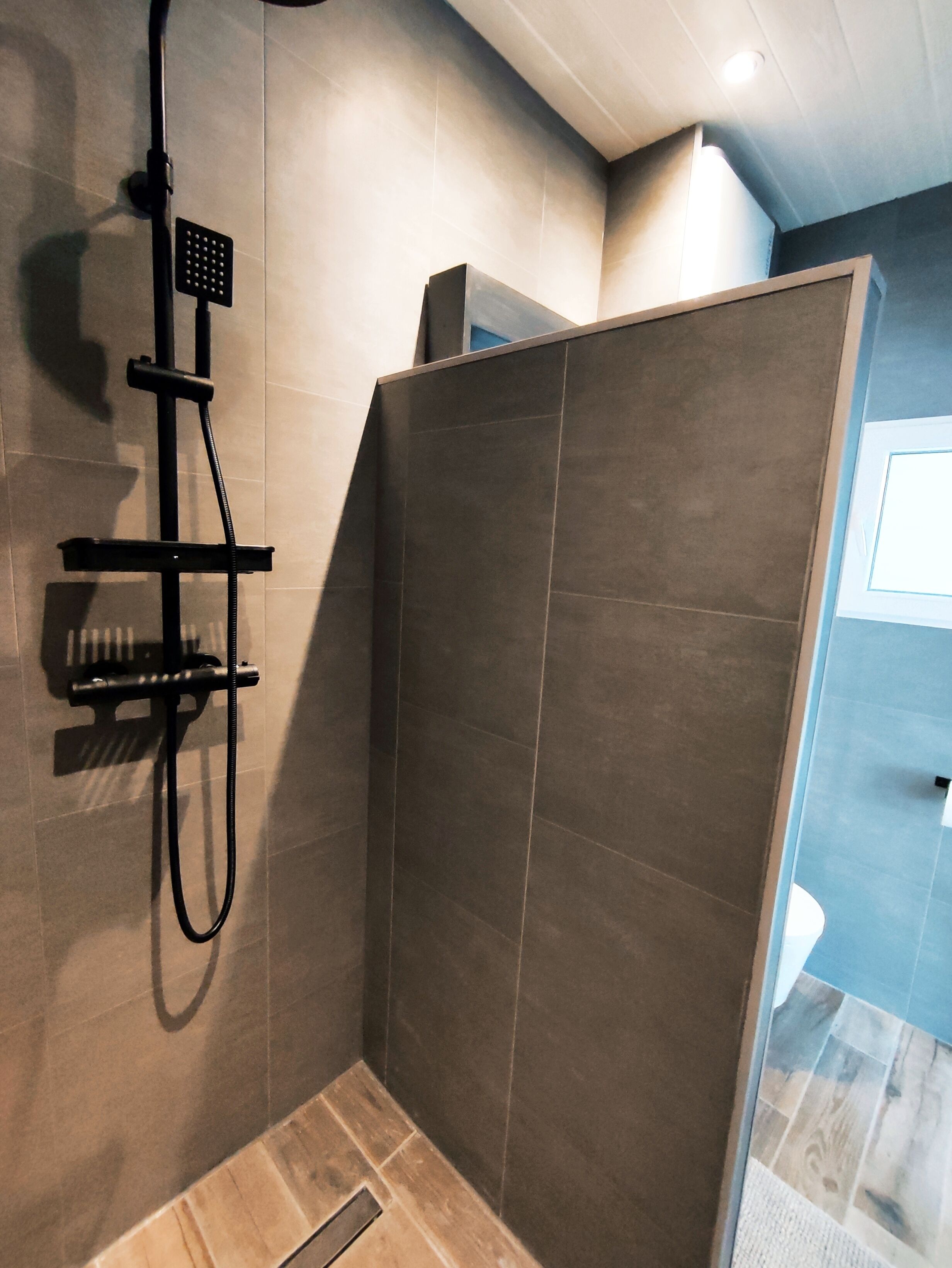 A modern shower area with a handheld showerhead and a fixed showerhead, tiled walls, and a wooden floor.