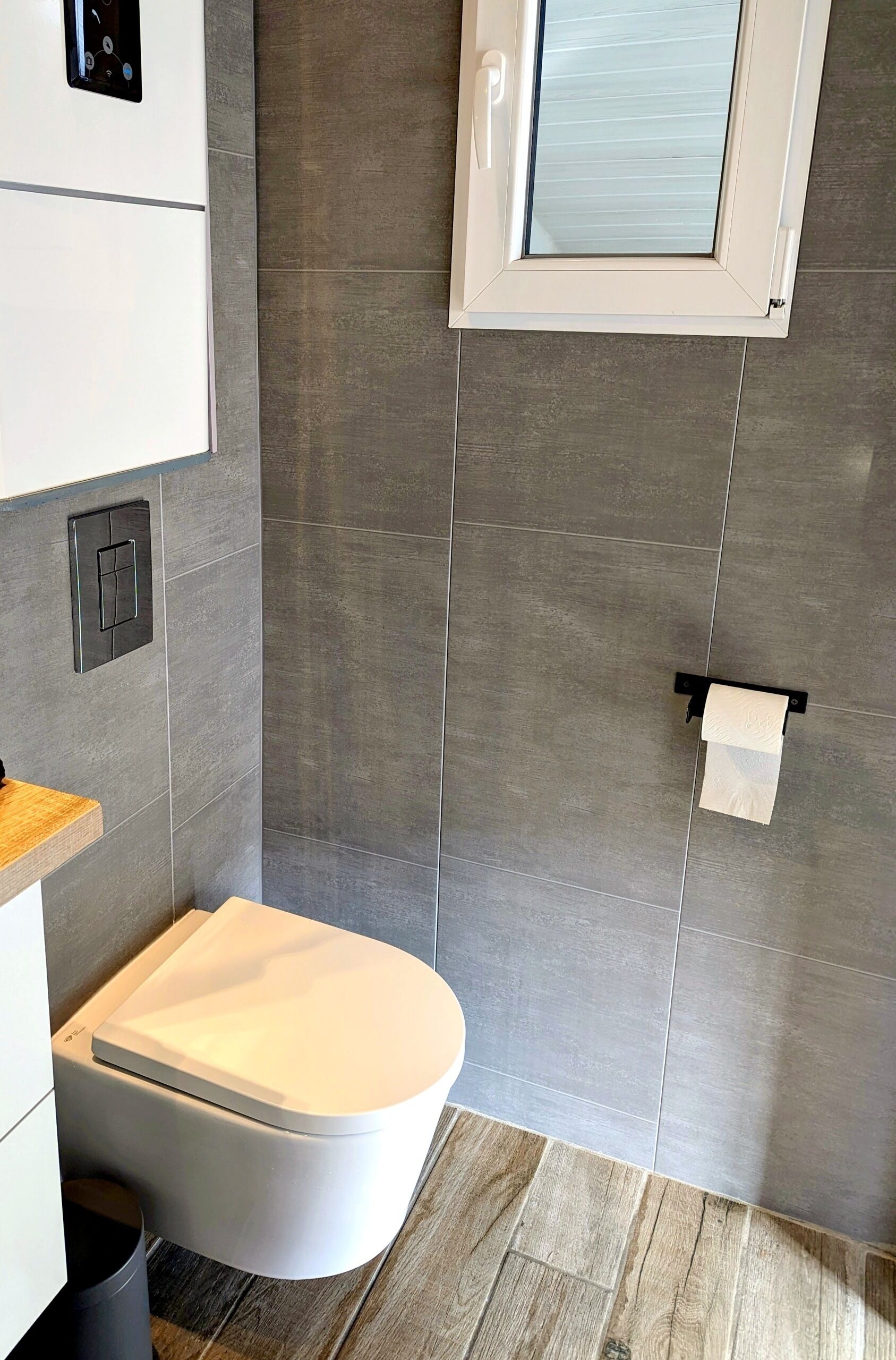 A modern bathroom with a toilet, a towel rack, and a window.