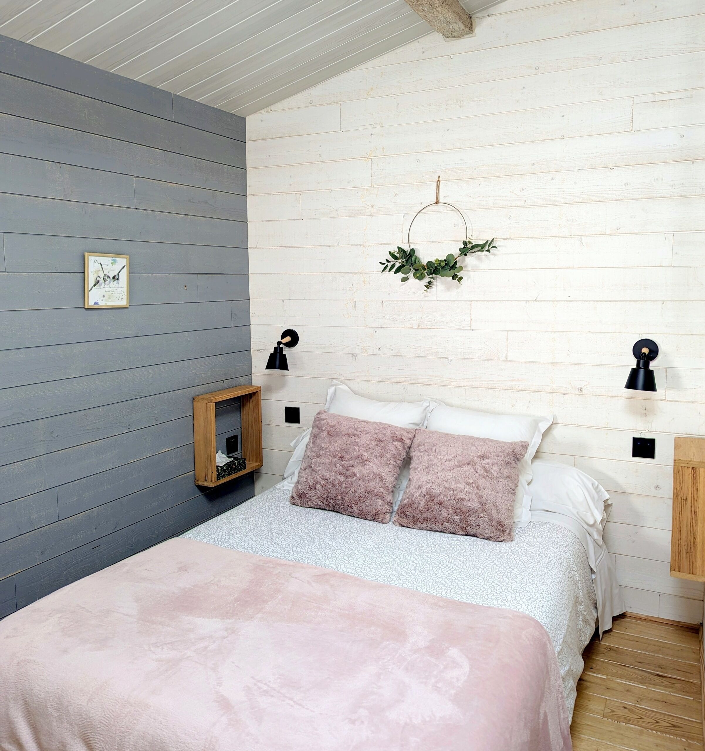 Een slaapkamer met een bed, twee wandlampen, een lijst met een afbeelding en een klein houten plankje.