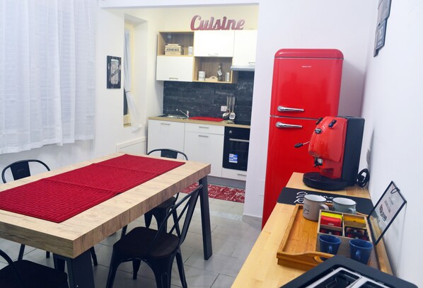 A compact kitchen with white cabinets, a red refrigerator, and a coffee machine.