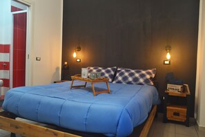 A bedroom with a bed, a bedside table with a lamp, a nightstand, and a storage box.