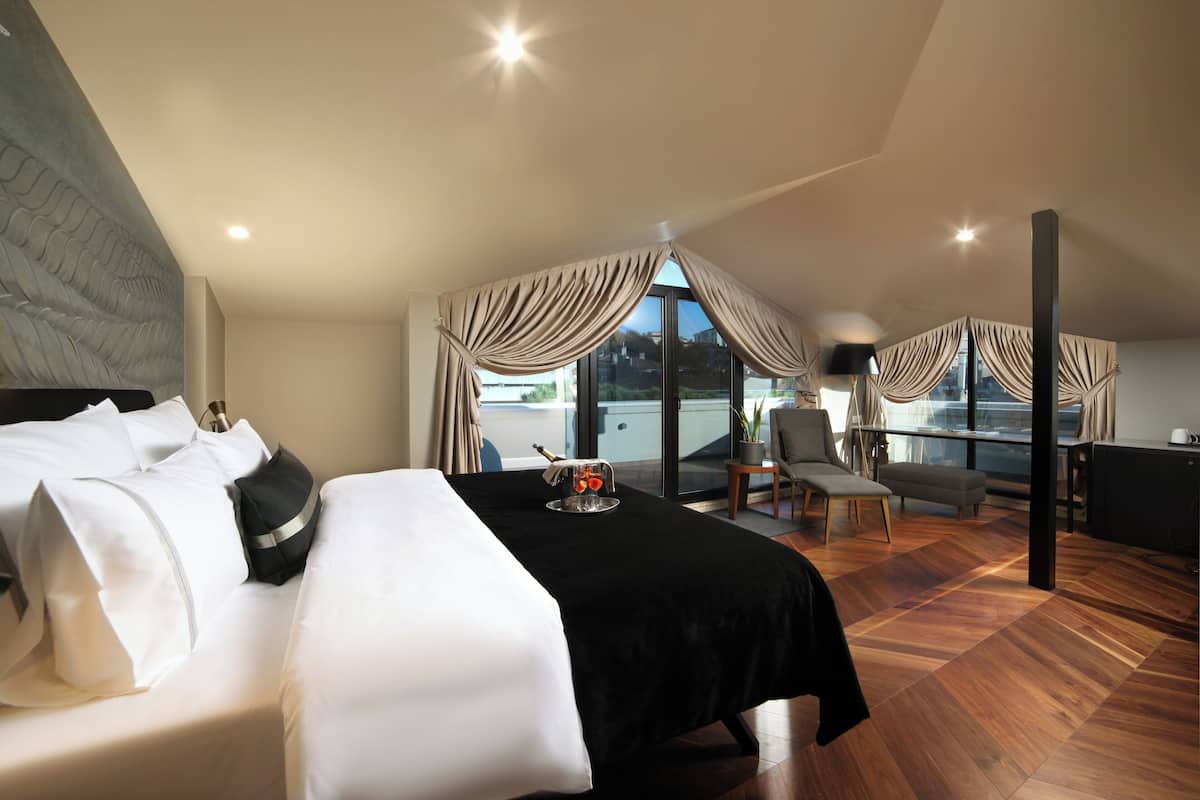 A modern hotel room with a large bed, a dining area, and a view of the city.