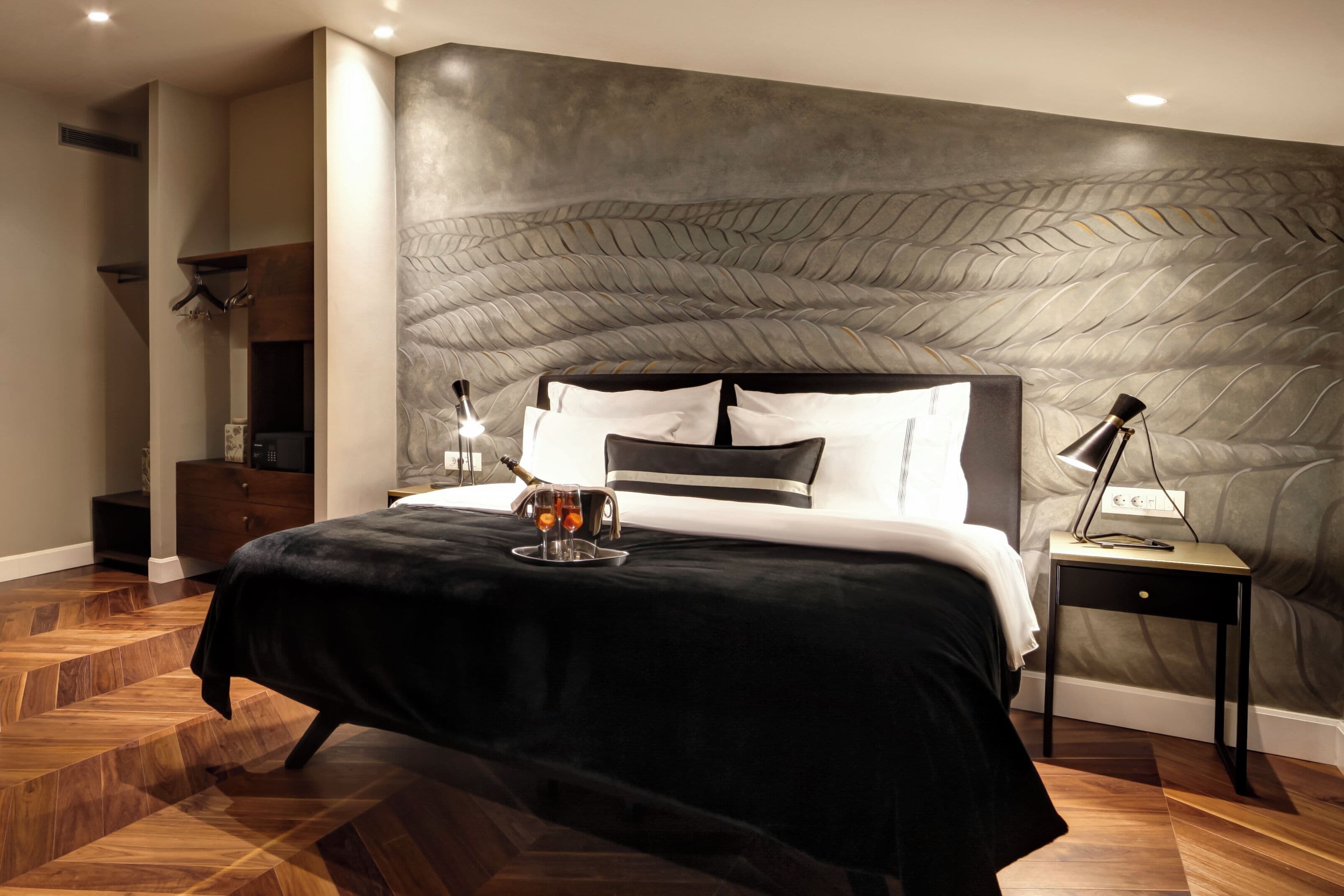 Quarto moderno com uma cama grande, mesa de cabeceira com abajur e bandeja com garrafa e copos.