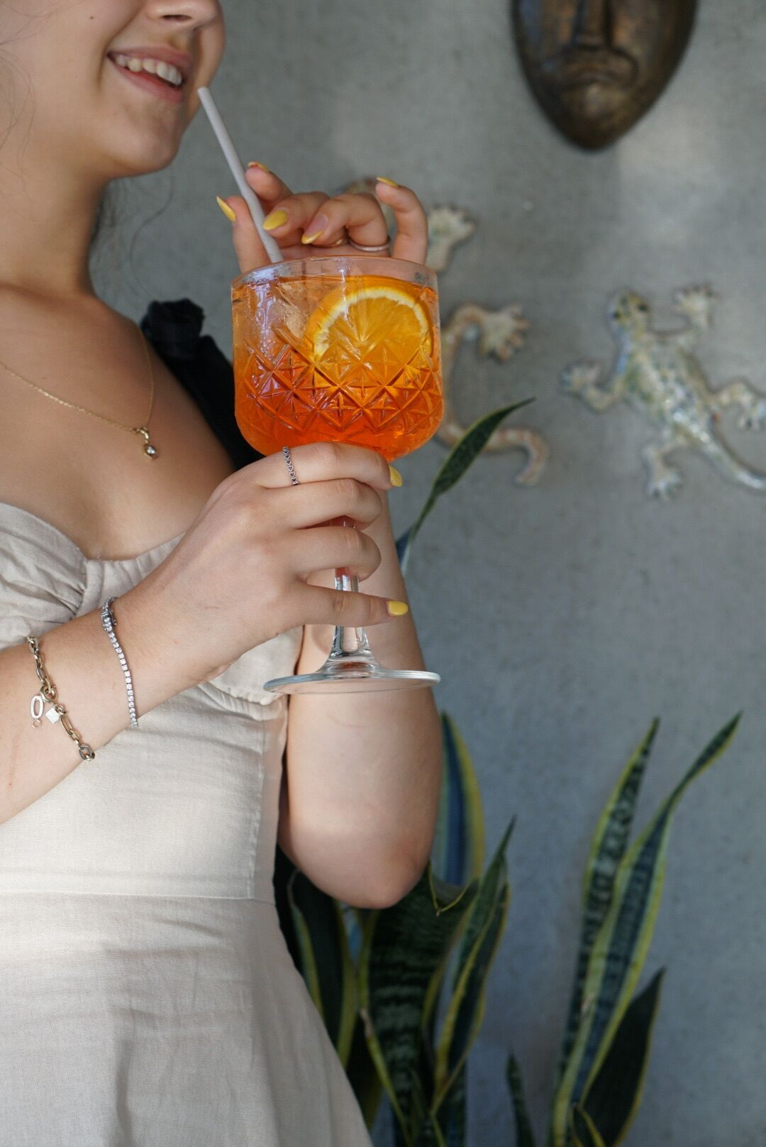 Uma pessoa segurando um copo com canudo, contendo uma bebida com uma fatia de laranja.